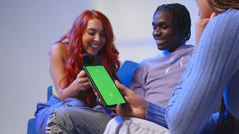 Close-Up-Of-Woman-With-Green-Screen-Mobile-Phone-Sitting-With-Gen-Z-Friends-Talking-And-Sharing-Posts-1